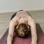 A woman in a child's pose during a yoga session on a red mat indoors, promoting relaxation and wellness.